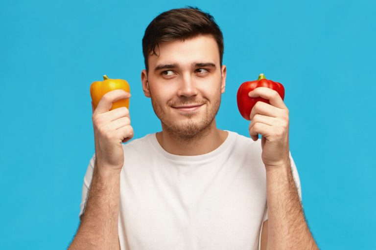 Mann hält gelbe und rote Paprika in den Händen, fragender Gesichtsausdruck.